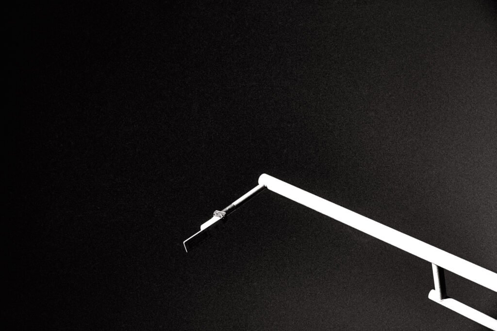 A high contrast b&w photo showing a metal light pole extending diagonally into the frame, against a nearly black sky